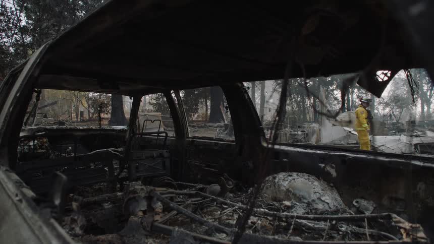 Charred vehicle wreckage allows view of firefighter examining debris