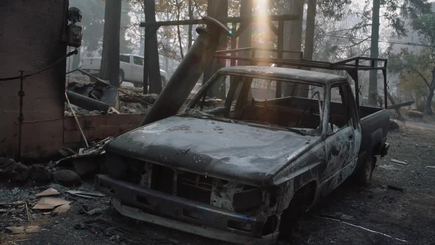 Sun shines onto burnt and damaged ruined building and pickup truck near foggy conifer forest