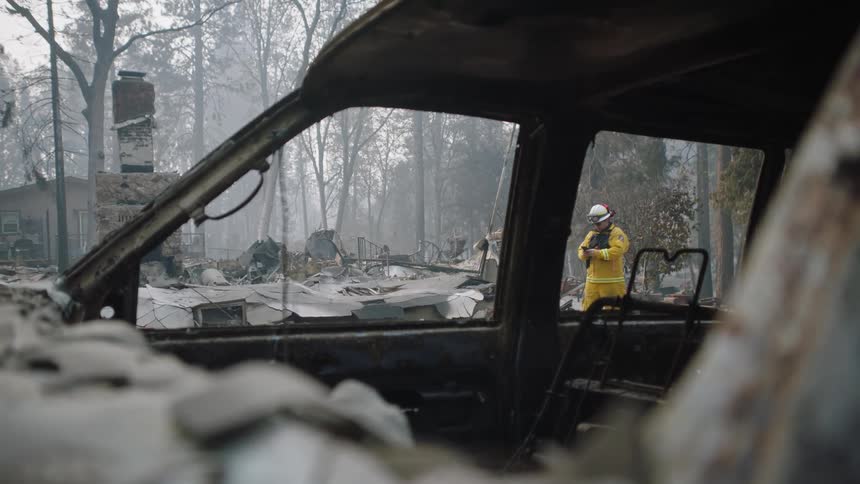 Firefighters wearing yellow protective gear inspect the damages on an area burnt by wildfires