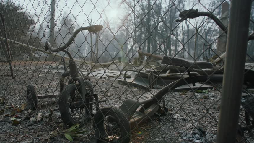 Childrens tricycles inside a fenced in area with a dilapidated playground