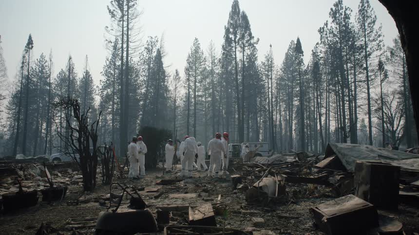 A group of workers in white suits stand around looking at rubble on the ground