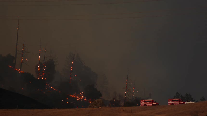 The wildfire burns and flames high in trees glow as rescue vehicles are on the scene