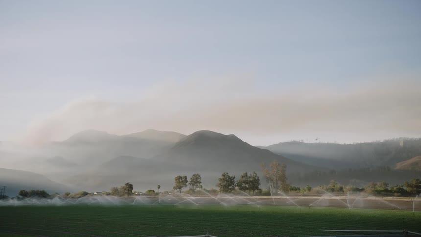 Panoramic view of mist rolling over the mountains next to the fields