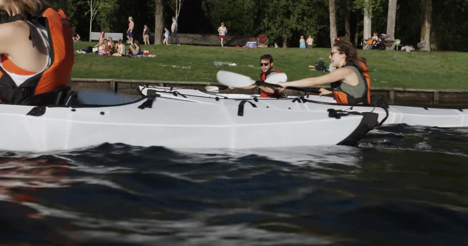 A group of friends rows kayaks past a park-like shoreline