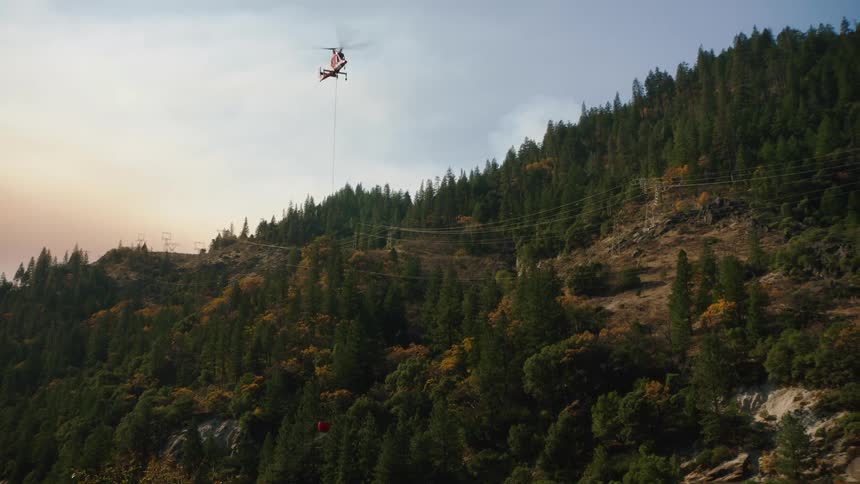 A helicopter flies above a forest as it dumps water