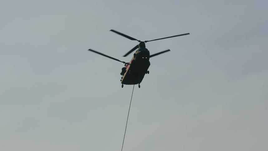 A helicopter carries a specialized bucked suspended on a cable to deliver water for aerial firefighting