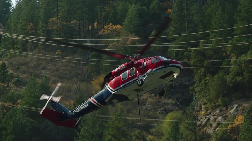 A helicopter hovers over a lake in the mountains to collect water for aerial firefighting