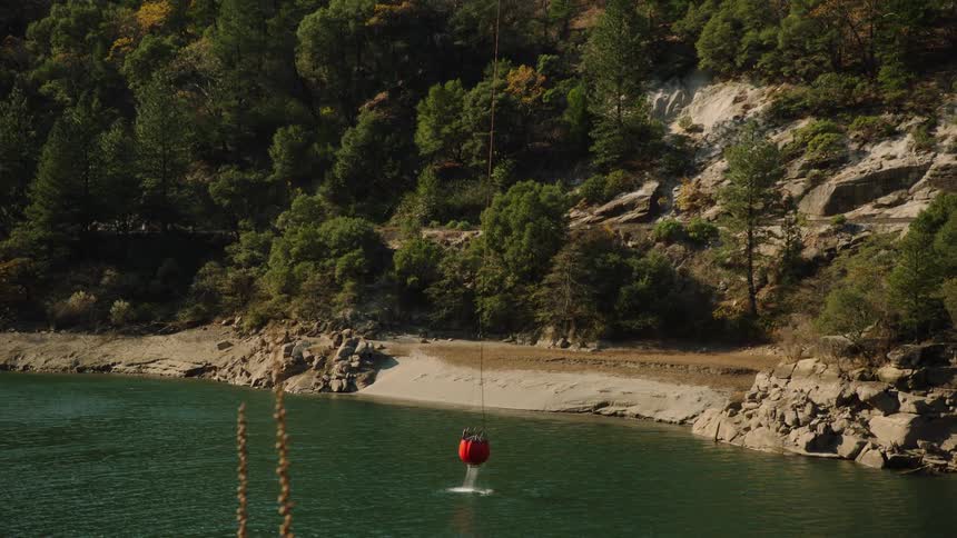A red bucket submerged in water and then being raised and carried away on a cable