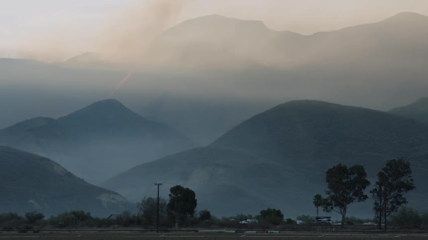 Wildfires burning the forests on a mountain range covered in smoke at morning