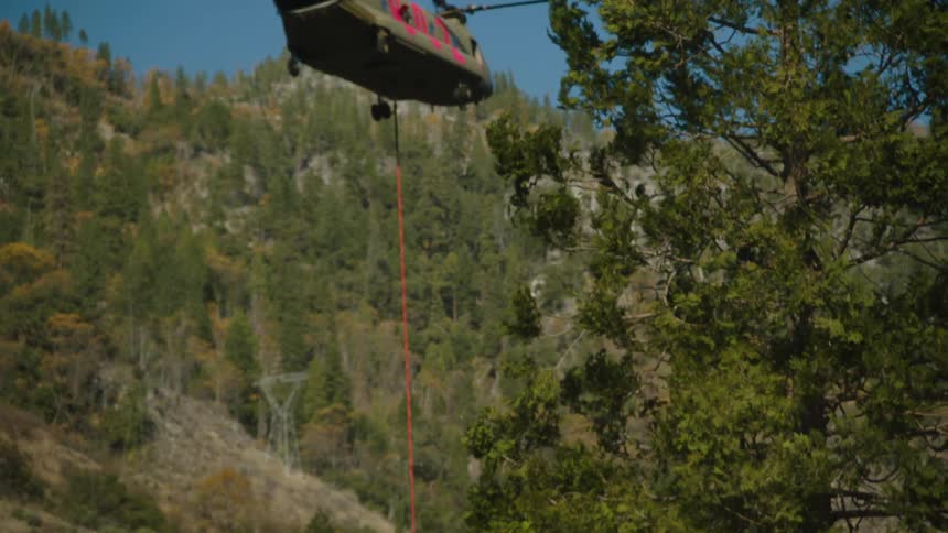 A helicopter lowers equipment to a firefighter in the woods