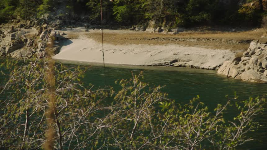 A bucket being lowered into river water then raising as a helicopter flies away from the river