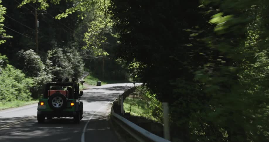 Green jeep drives down a winding road in the middle of the woods