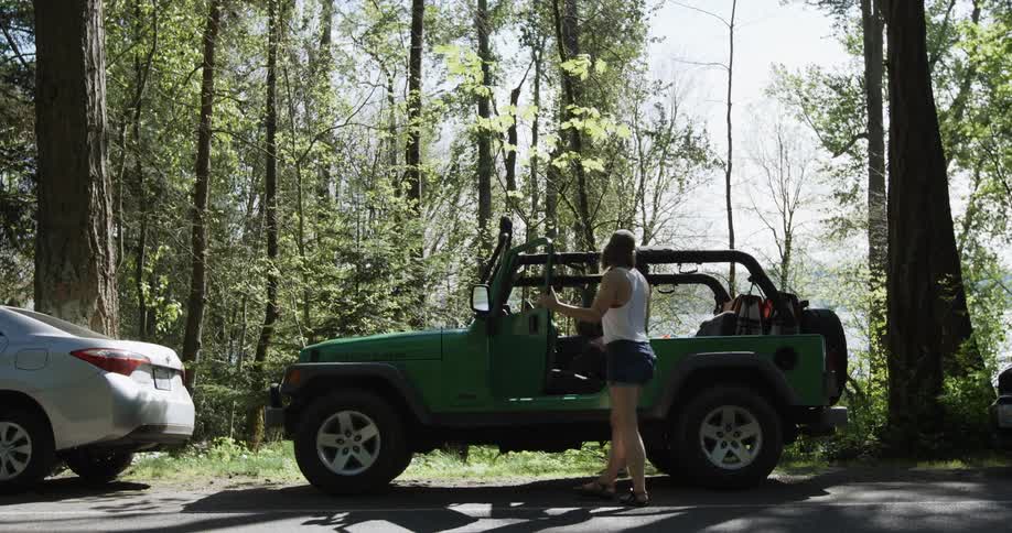 Two people get out of a green jeep in the woods