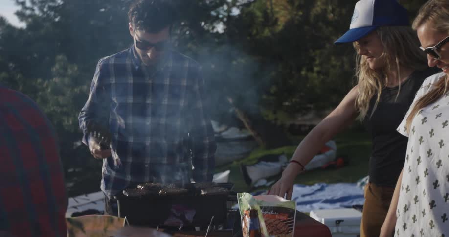 A group of friends gathered around a small grill in a park setting