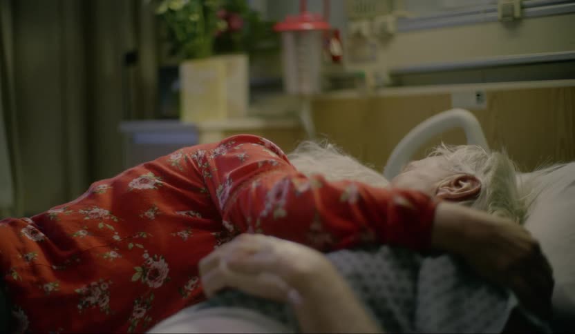 A woman holds a mans hand while he lays in a hospital bed