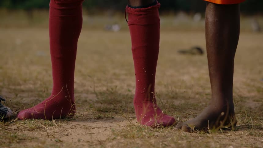 Close up of the feet of barefoot men standing on a field at daytime