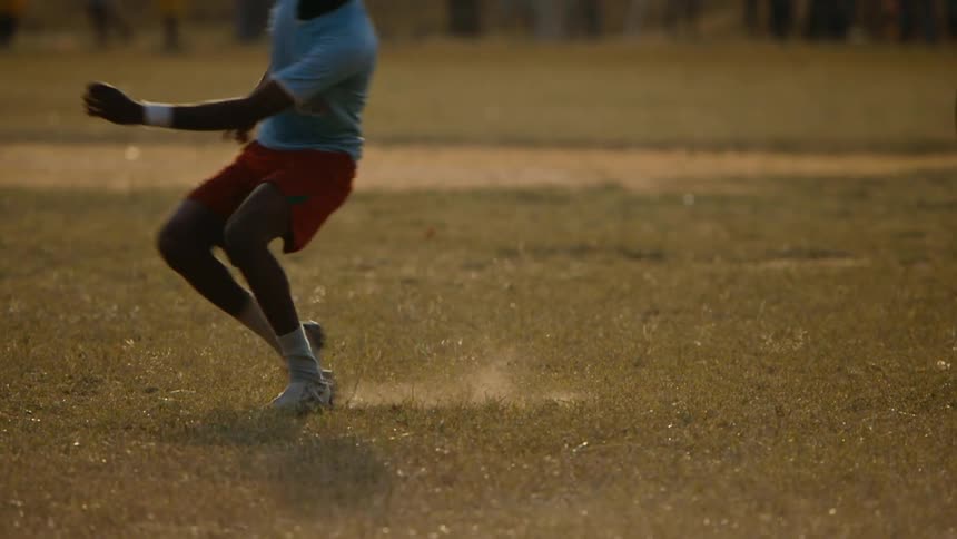 A soccer ball sits on the grass as a boy runs up and kicks it across the field
