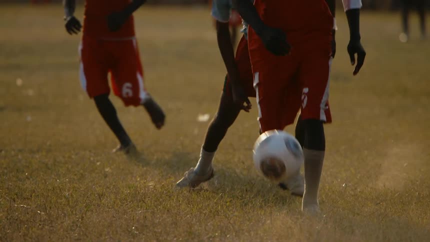 Barefoot man playing a soccer match on a field kicks the ball