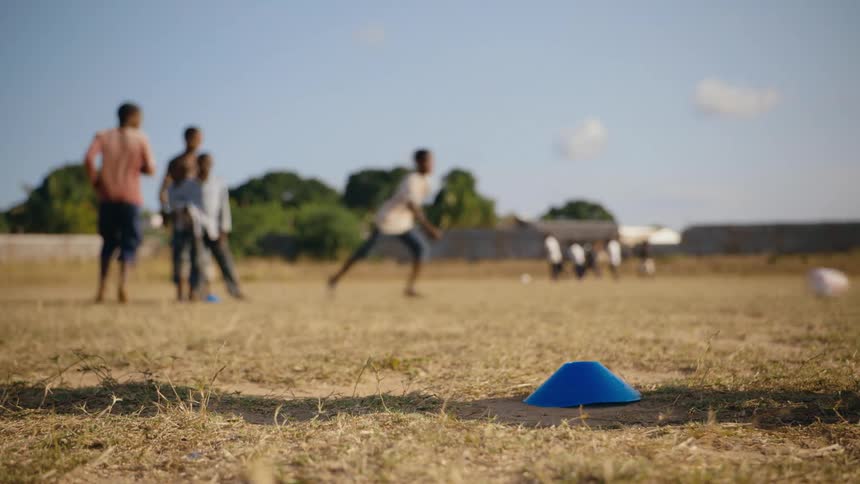 Close up of a barefoot teenager practicing soccer on a field with friends