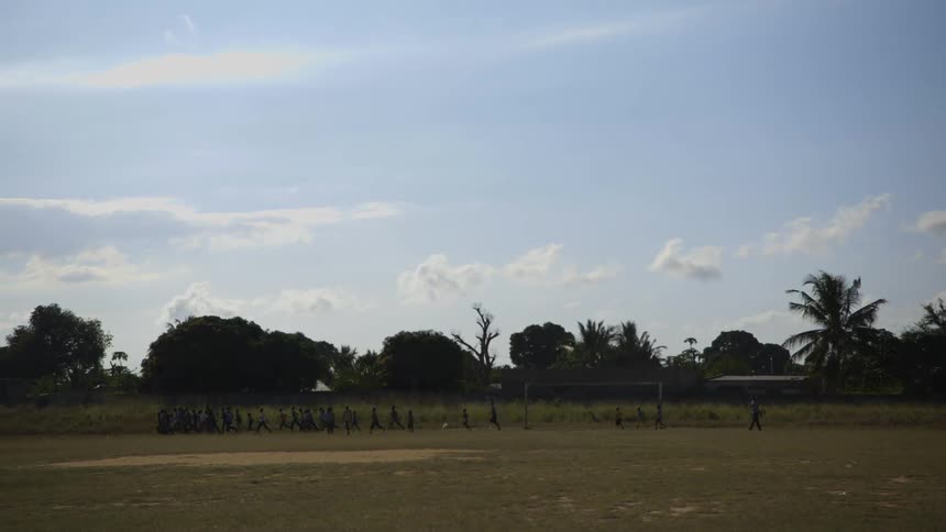 Youths run in group along edge of soccer field
