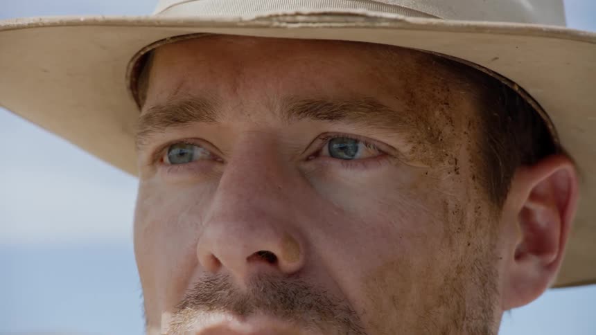 Close up of cowboy's dirty face as he sees something in the distance