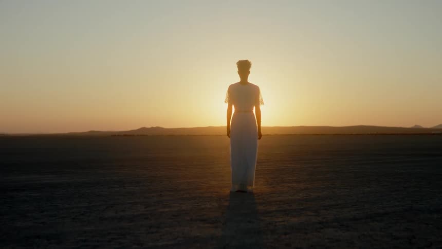 Woman walking on a field towards the sunset
