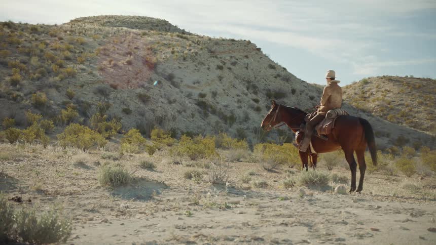 Cowboy rides up to a hill in the desert