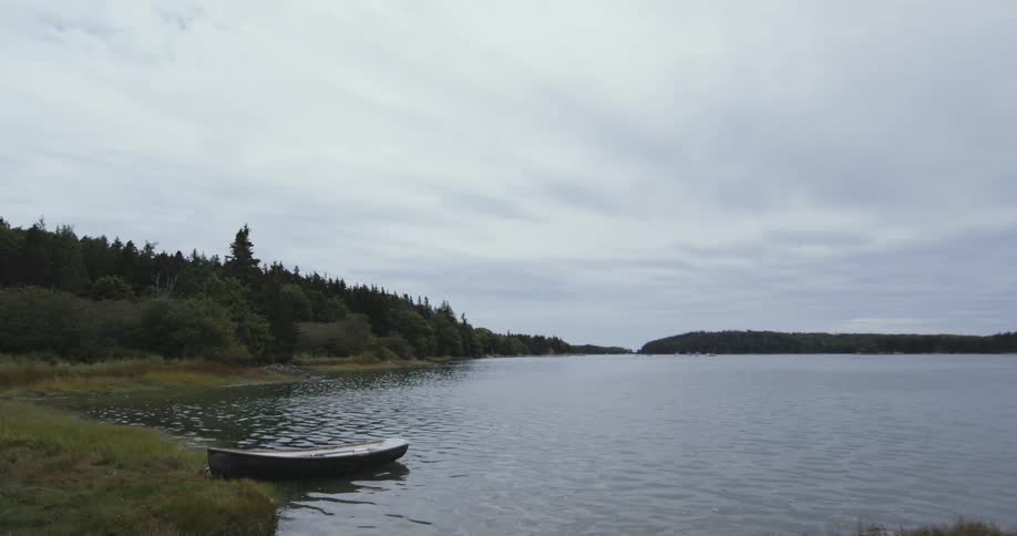 A lake shoreline with a boat parked on the bank and forests cover the shoreline