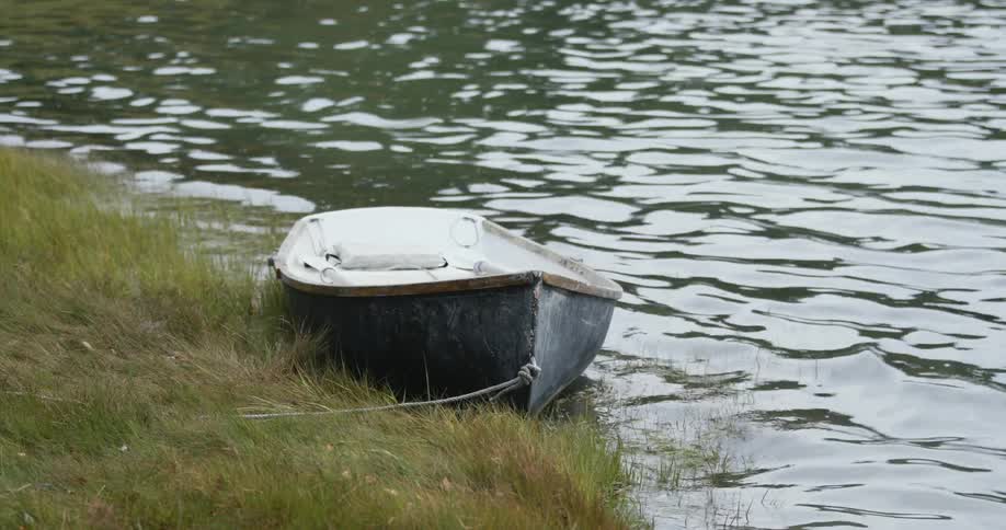 A small boat resting along the coast rocks as the river water ripples and waves