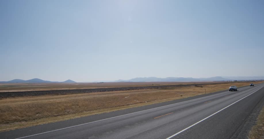 Panoramic view of vehicles driving on a road through the desert at daytime under a blue sky
