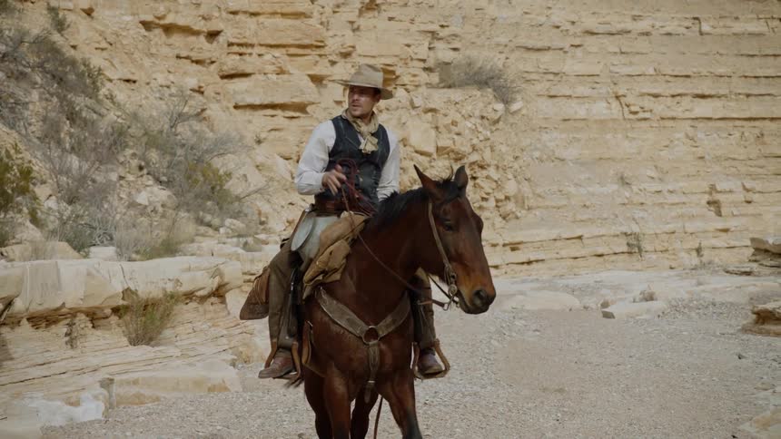 Cowboy riding in on a horse then getting off taking off hat and looking around