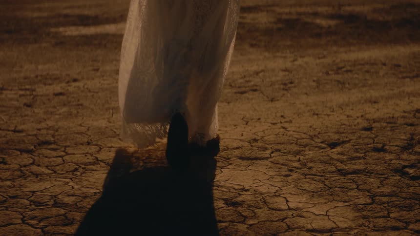 Young woman wearing a white dress walking through the desert at evening