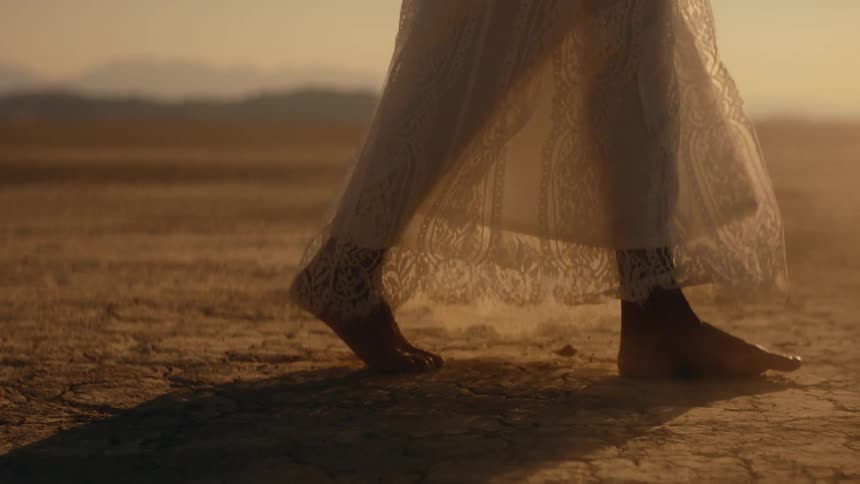 A persons bare feet as they walk across desert ground