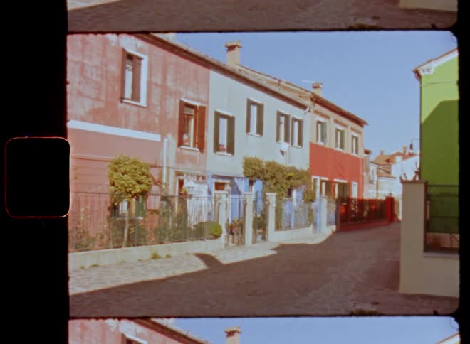 A small street or road with colourful rowhouses painted in different and bright colors shining on a bright sunny day in a Mediterranean city in southern Italy on Super 8 film
