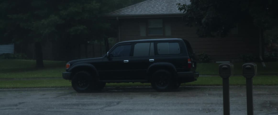 A black truck is parked in front of a house on a neighborhood street as rain pours down