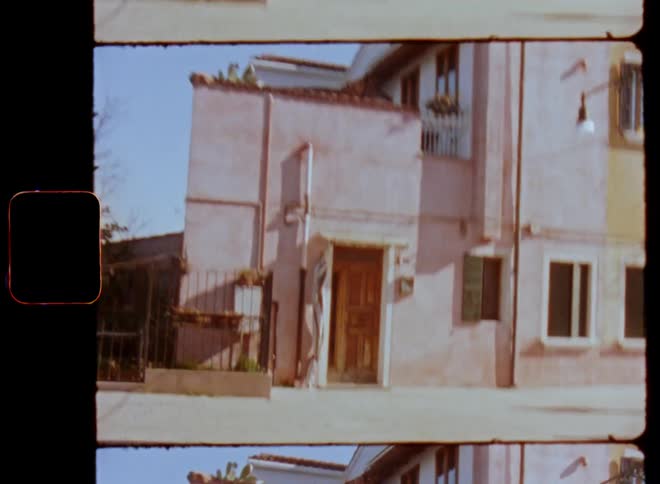Walking towards or approaching a home or house with wooden door standing next to a small street in an old city or village with vintage buildings filmed on retro Super 8 footage