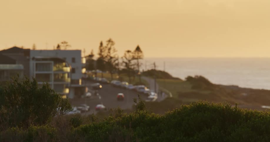 A house overlooking the ocean with a road winding up around the house with cars traveling on it