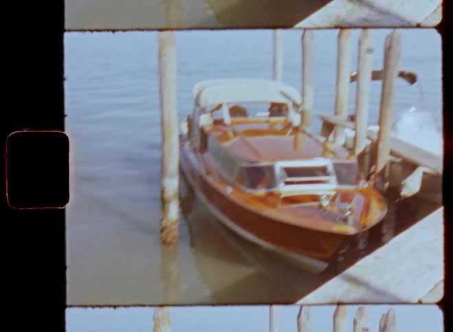 Walking up to a wooden paneled motorboat that is parked as it floats near posts at dock in a harbour or port ready for a boat ride on a sunny day on vintage film