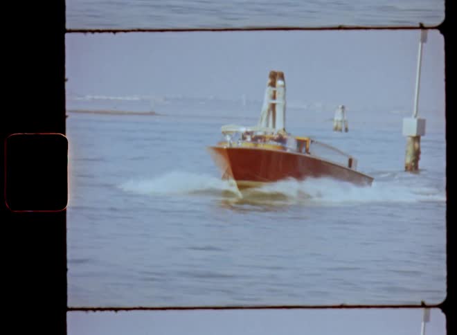 Dynamic Super 8 film footage of a wooden motor boat driving or racing at high speed through ocean waters between poles in the water marking the waterway that pass by fast on sunny day with blue sky