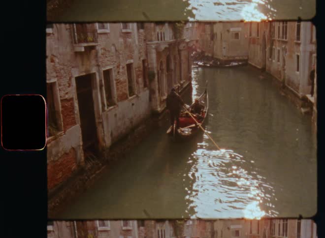 A man is rowing his canoa or riding a gondola in a flooded street or canal in a town with decrepit and run-down buildings transporting guests or tourists on the waterway of this urban environment