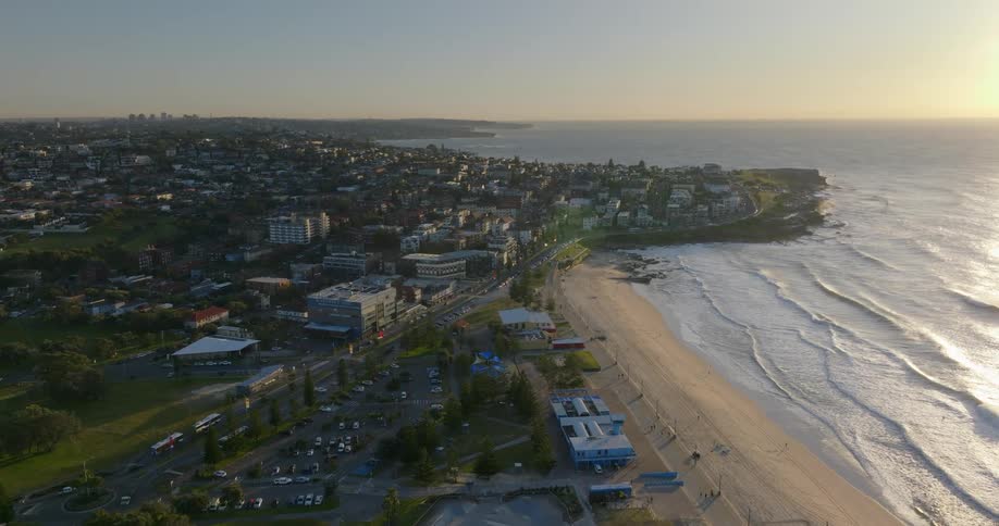 An aerial of a coastal city with waves rolling onto the sand buildings and houses along the beachline