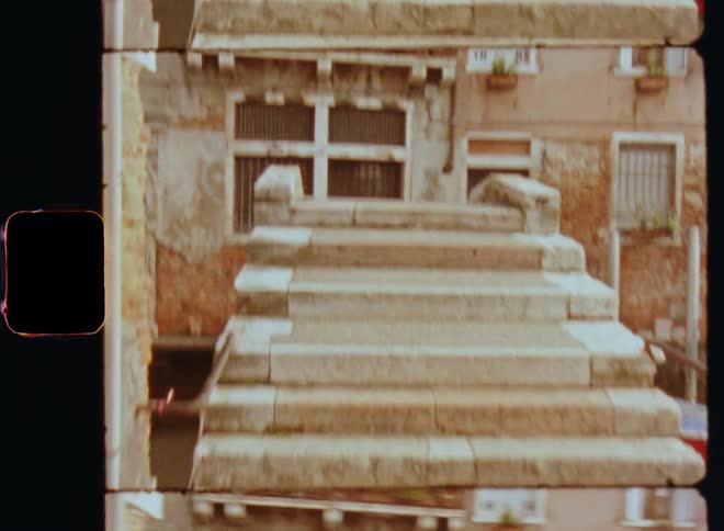Vintage Super 8 POV footage walking with shaky steps over a concrete bridge approaching the stairs or staircase leading the way over the water of the small canal or waterway