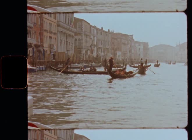 Several Venetian gondolas floating or swimming on Venice canals transporting people and other items on a gloomy morning with bright gray sky in the 1980s caught on vintage film footage