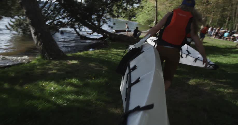 People carry kayaks near a lake