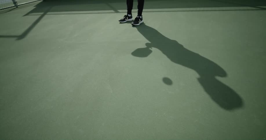 Person bouncing ball on paddle casts shadow onto court