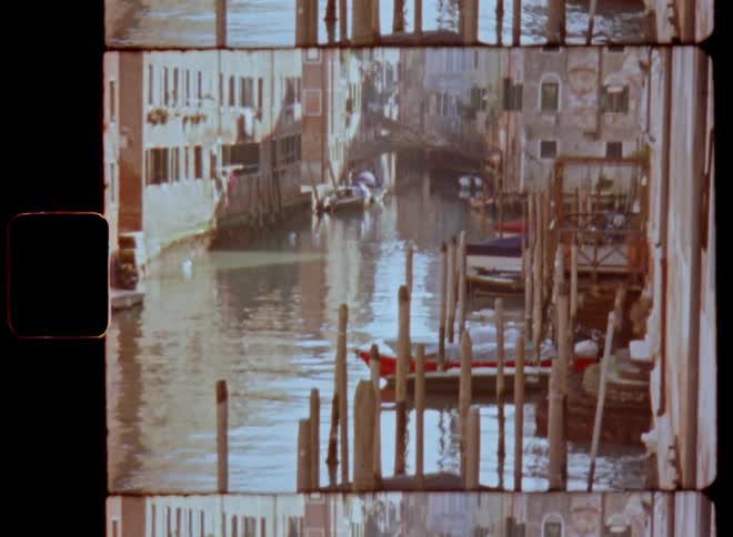 Idyllic Super 8 film footage of a canal in an old town or historical city center with boats piers wooden platforms and houses and buildings with lots of windows as the sun shines brightly on a warm summer day