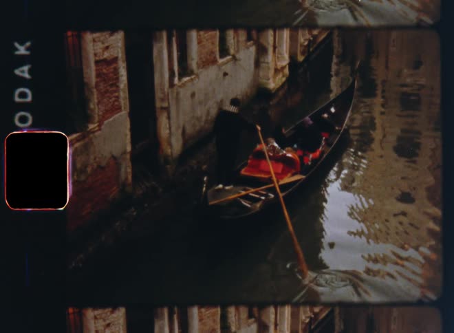 A standing man paddling a Venetian gondola or canoe boat through a small canal transporting two guests travellers or tourists to their destination while enjoying the boat ride through the old city center on vintage Super 8 film