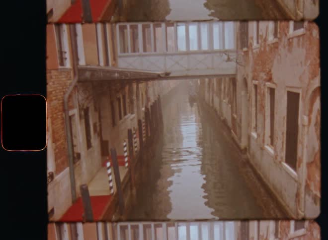 A view of an enclosed bridge with windows over a narrow canal in Venice surrounded by old brick walls with paint peeling of the stone walls on retro film