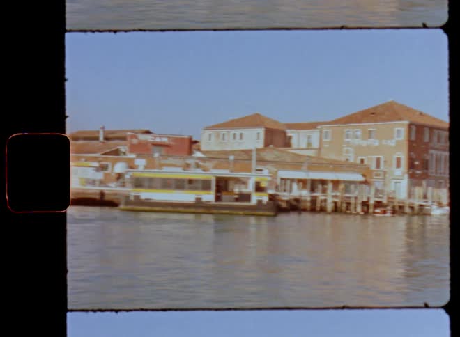 Enjoying a boat ride through a waterfront city on a sunny day with blue sky and bright sunshine passing large buildings and houses standing at the pier with small ships parked at the urban harbor at the edge of the lake or canal