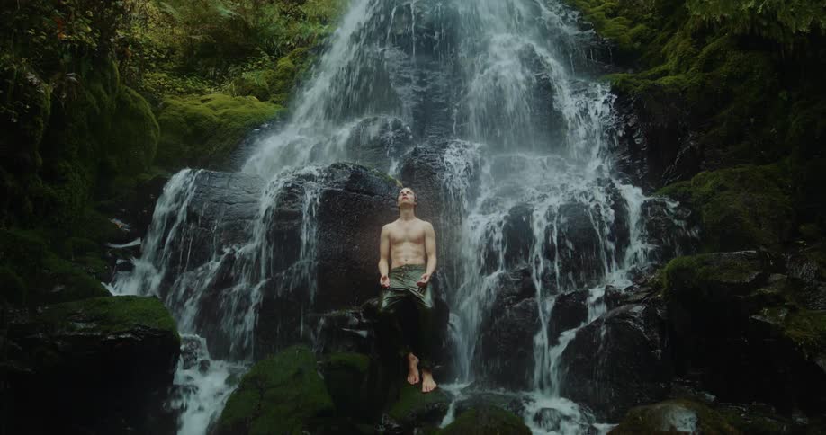 A man stands under a waterfall in a canyon